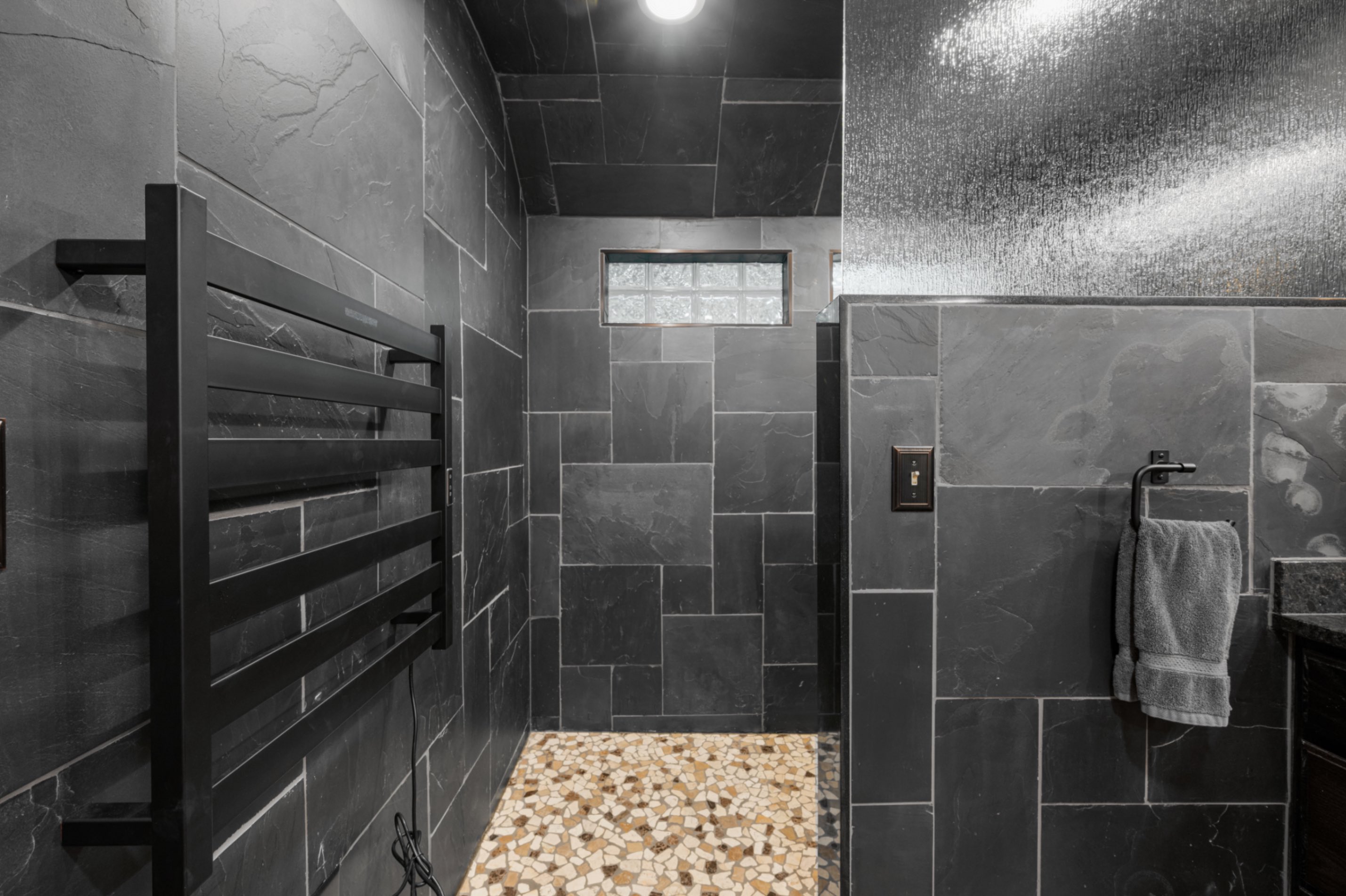 Walk-in shower with heated towel bar, glass block window, and pebble floor