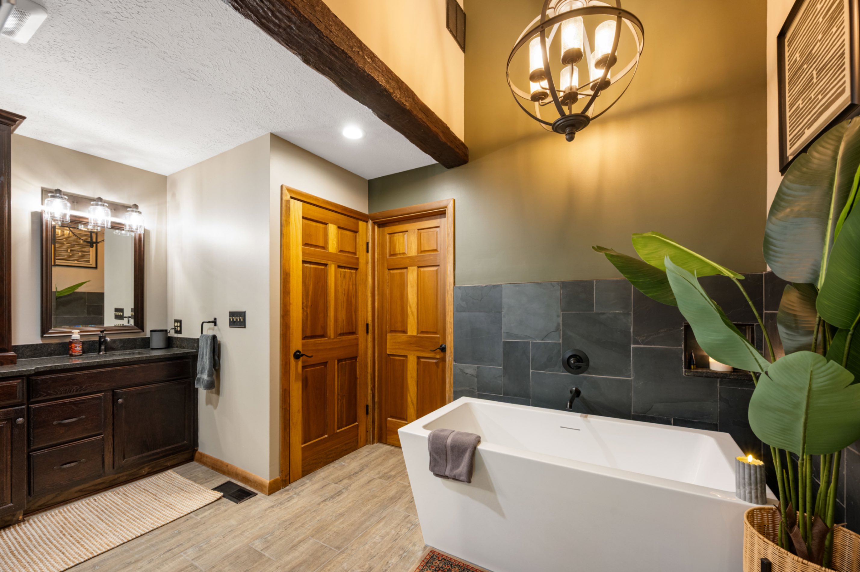 Full bathroom view — freestanding tub, vanity, wood beams, and pendant lighting